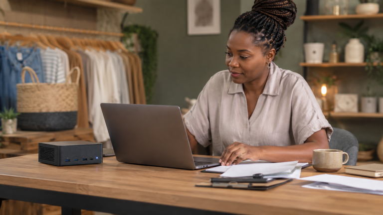 A South African boutique owner working at a laptop with a compact mini PC running local AI